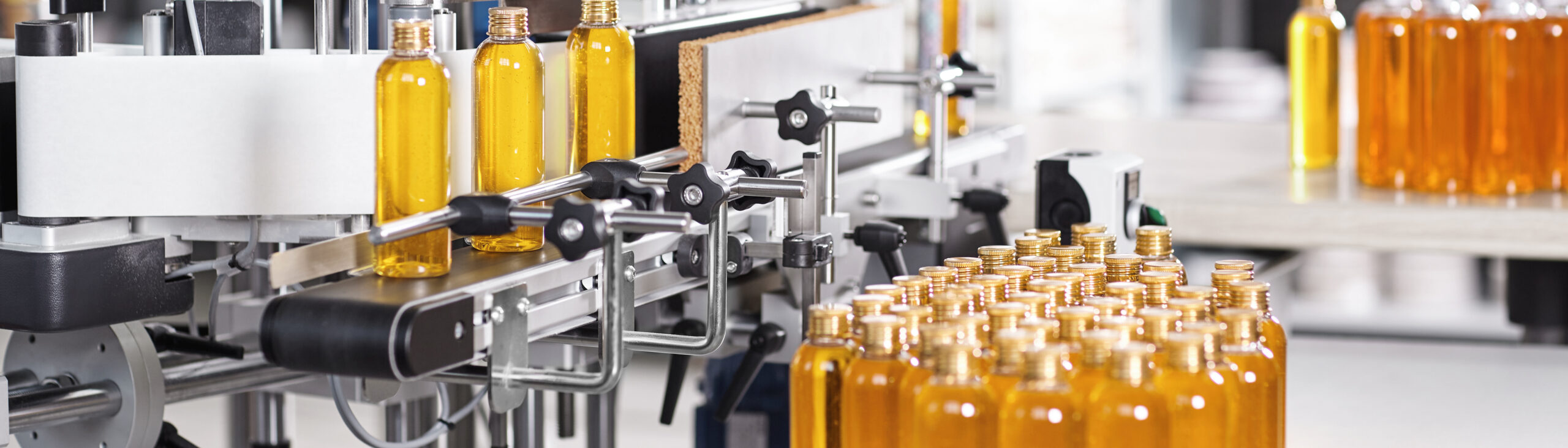 Bottles filled with soap yellow liquid standing on conveyor belt in factory. Automated process of creation soap on factory. Bottles with yellow thick substance standing in row going to be twisted
